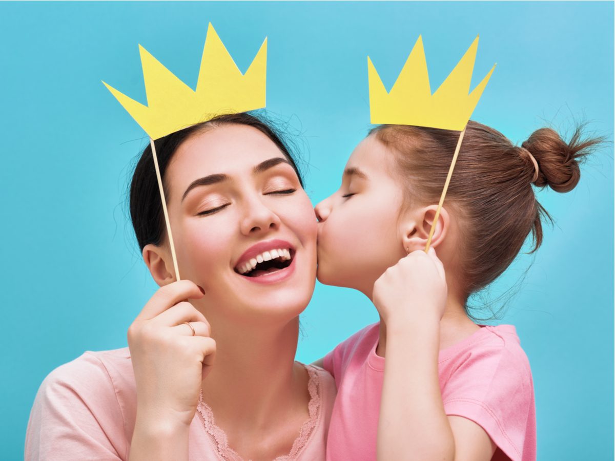 Daughter kissing mother while wearing paper crowns