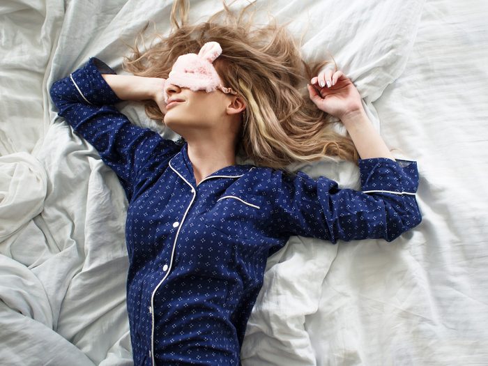 Woman in her bed in blue pajamas and sleep mask