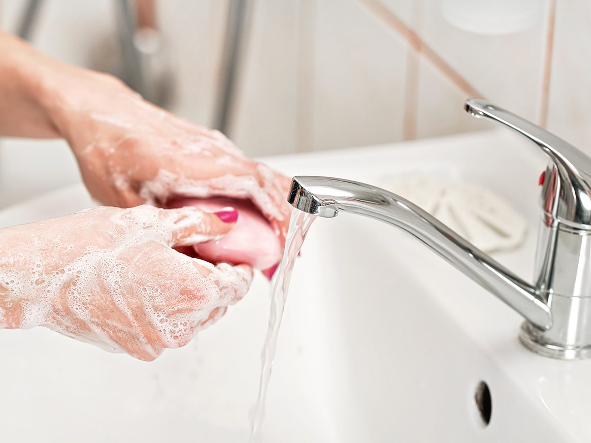 Person washing their hands under water tap faucet with pink soap bar. Detail on suds covered skin. Personal hygiene concept - coronavirus covid19 outbreak prevention