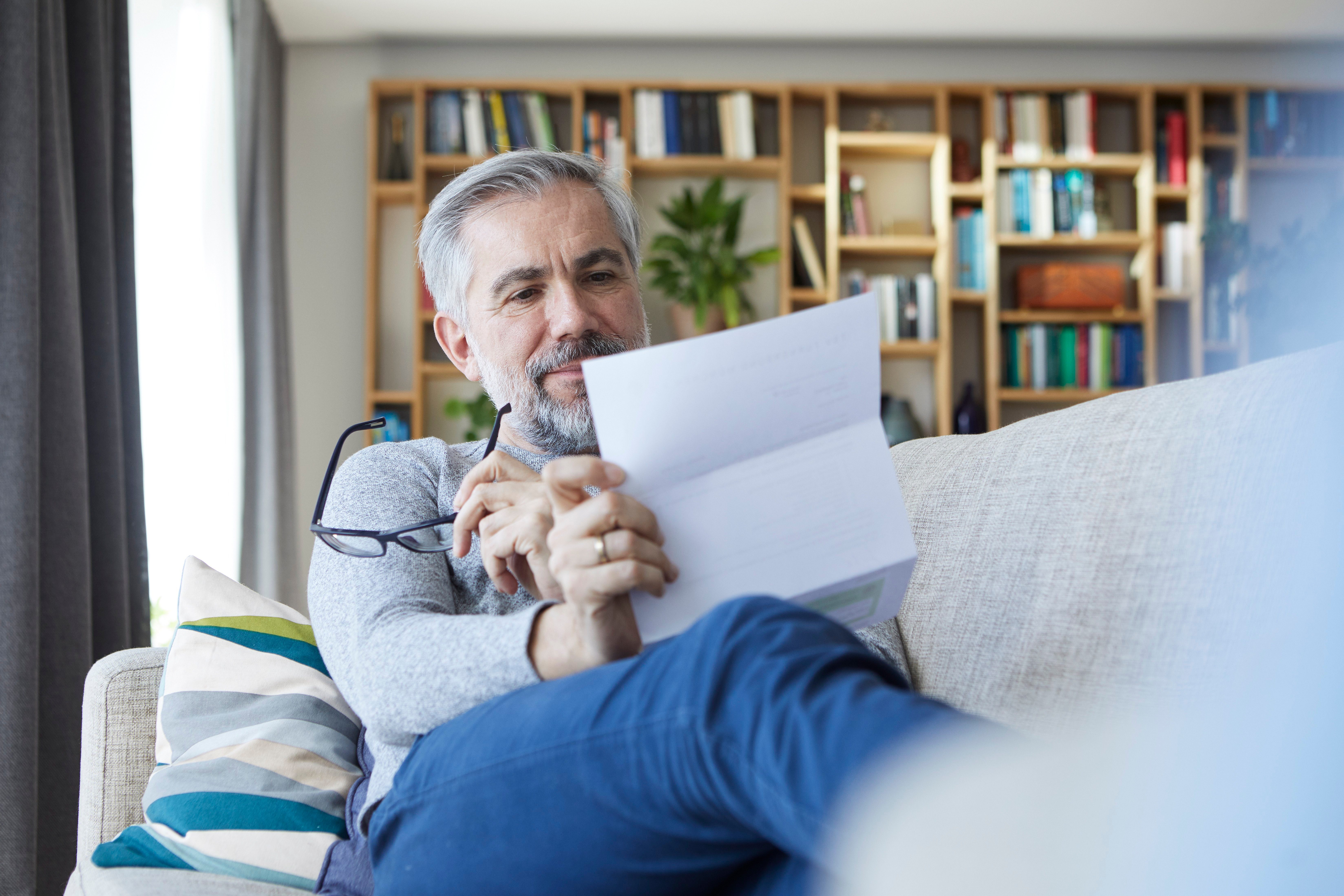 Mature man sitting on couch at home reading letter