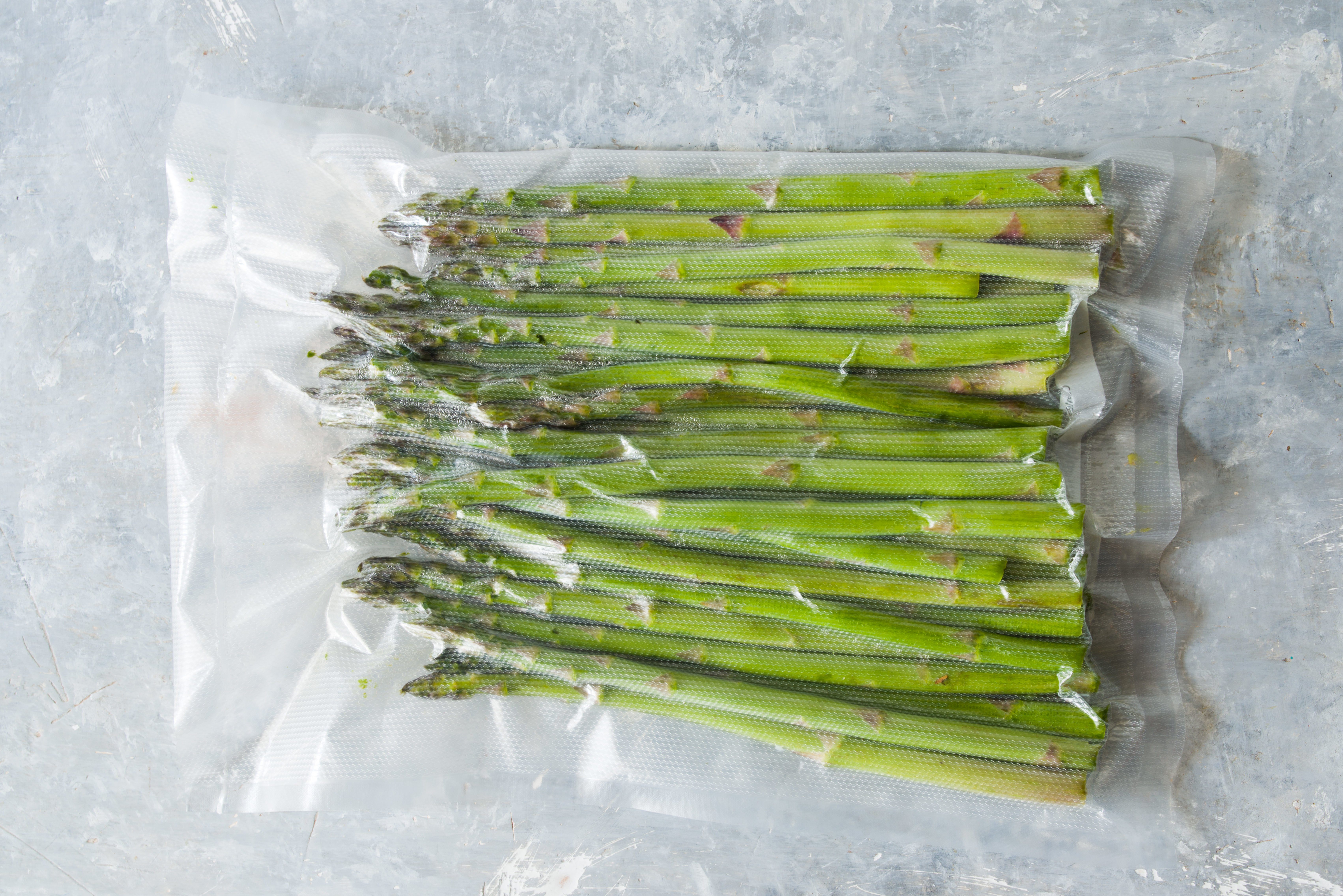 Vacuum sealed vegetables , asparagus, on a gray background top view, ready to be cooked with sous vide rooner