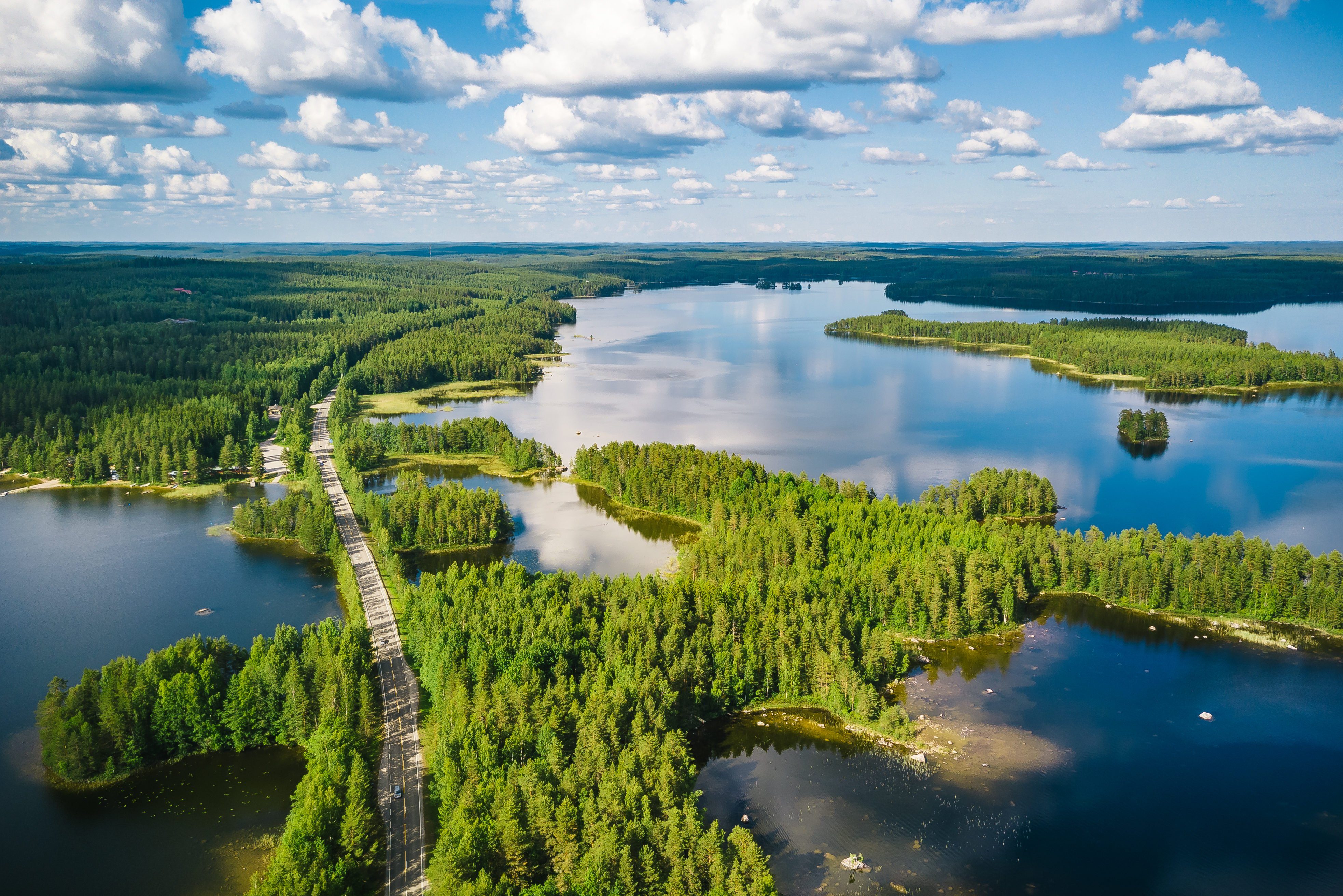 Aerial view of a winding road passing through forests & lakes in Finland on a summer day
