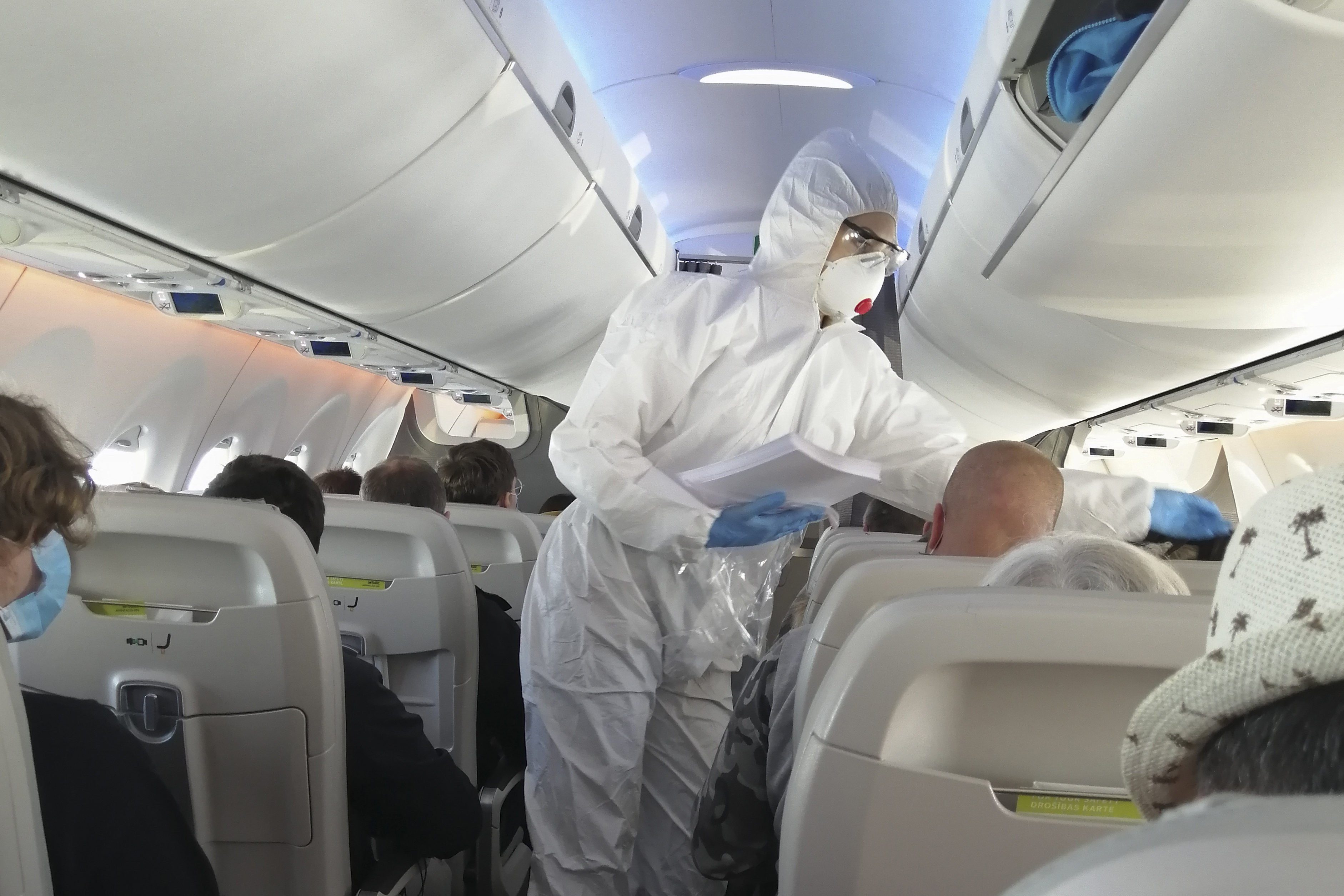 Stewardess in a white overalls and mask in the cabin serves passengers.