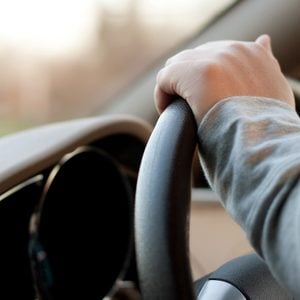 A woman holding the steering wheel of a car with one hand while driving.