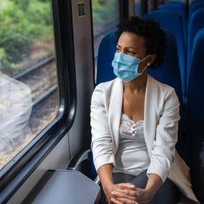 woman sitting on a train looking out the window wearing a face mask