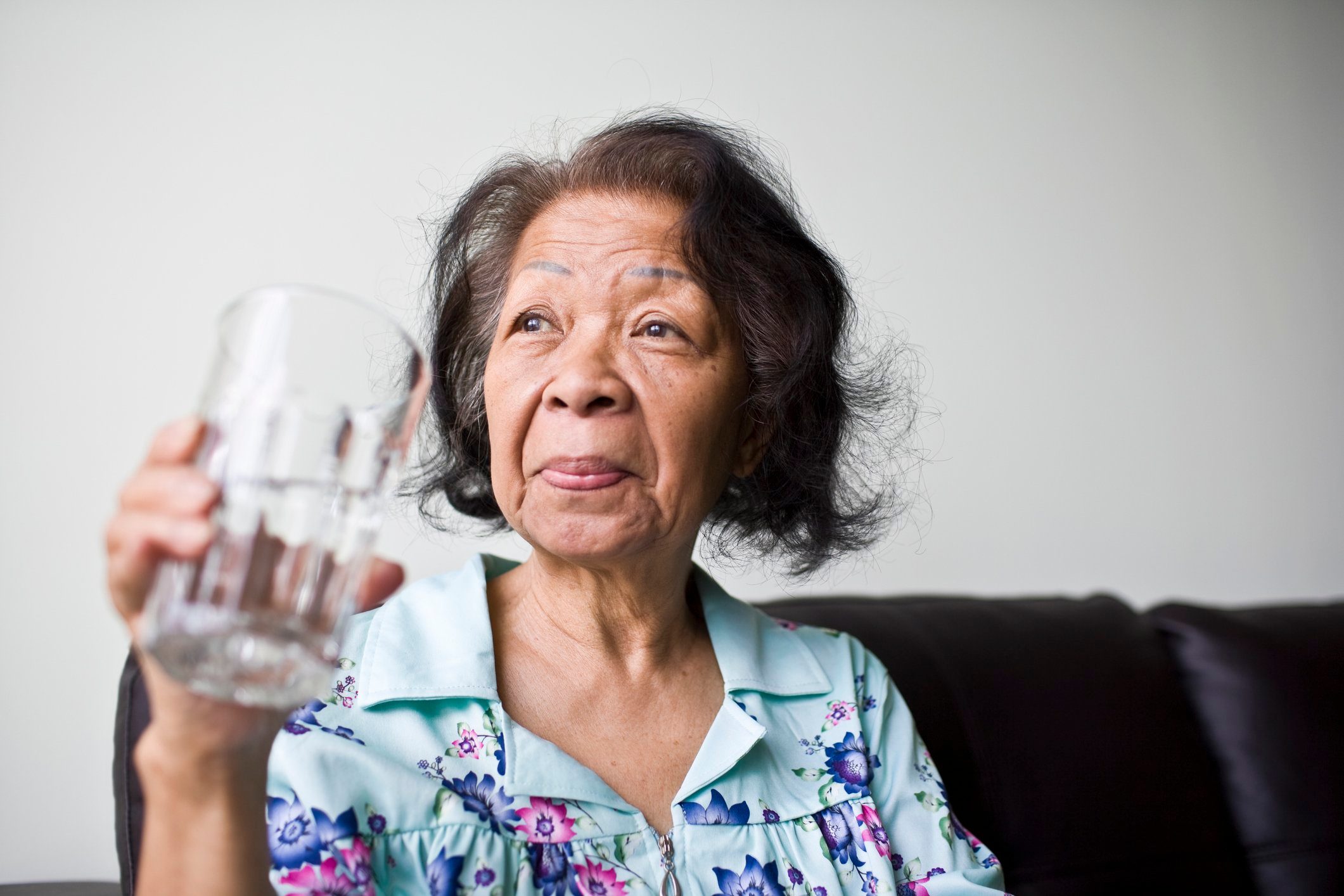 senior woman sitting on couch at home holding a glass of water