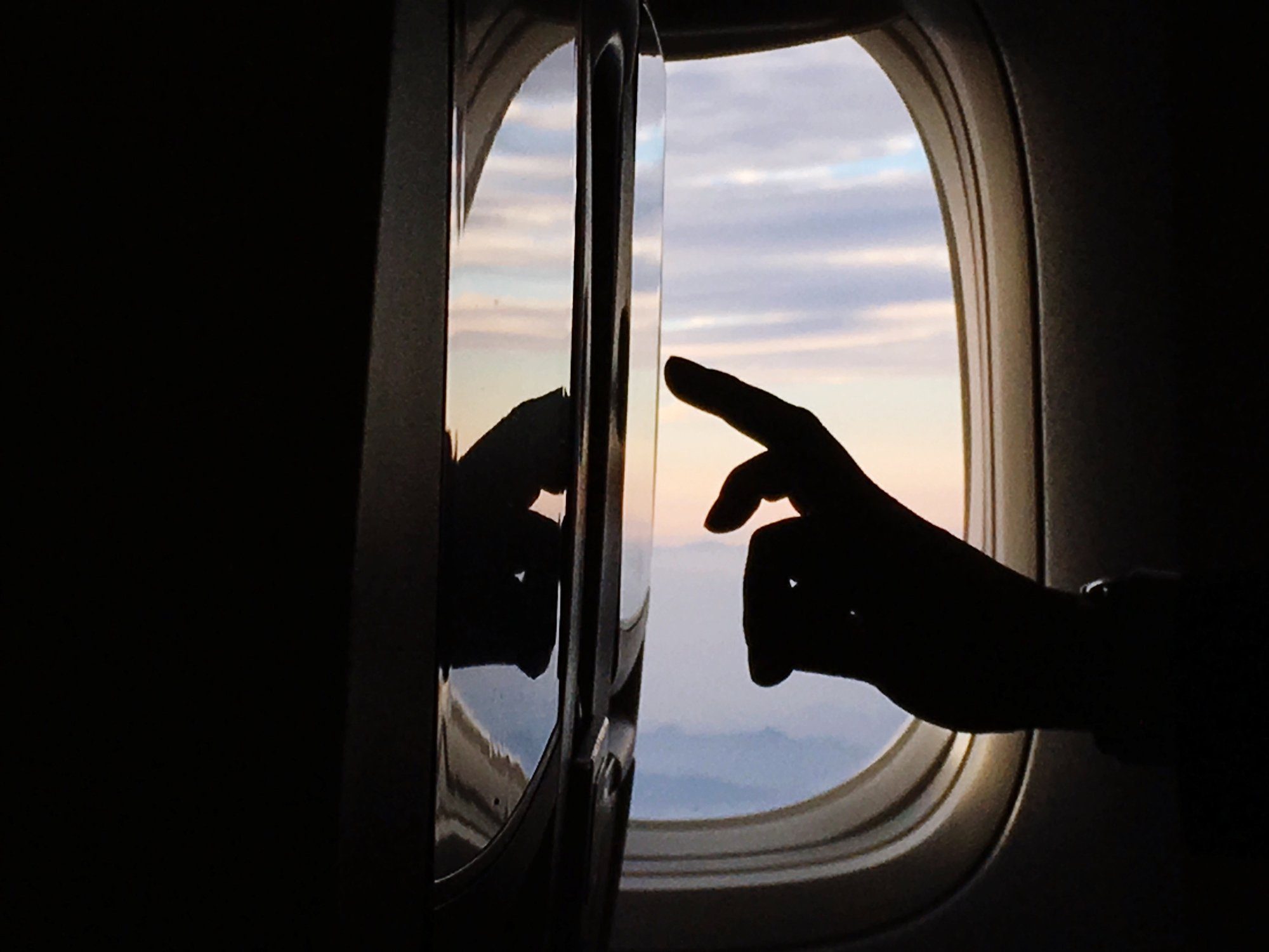 Cropped Image Of Silhouette Hand Touching Device Screen In Airplane