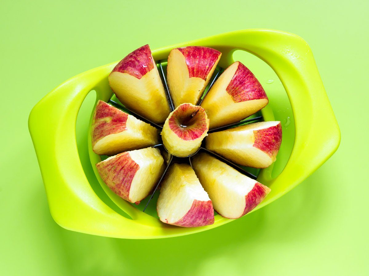 Apple on a green surface is sliced open with a green apple corer.