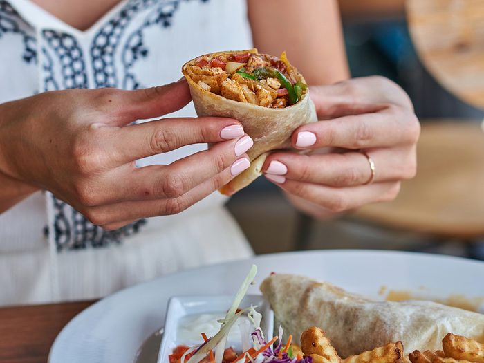 Nutritionists never order - Female hands holding tasty mexican burrito with different ingredients inside. Woman eating delicious pita and salad with French fried potato.