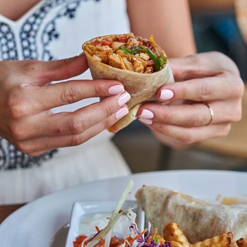 Nutritionists never order - Female hands holding tasty mexican burrito with different ingredients inside. Woman eating delicious pita and salad with French fried potato.