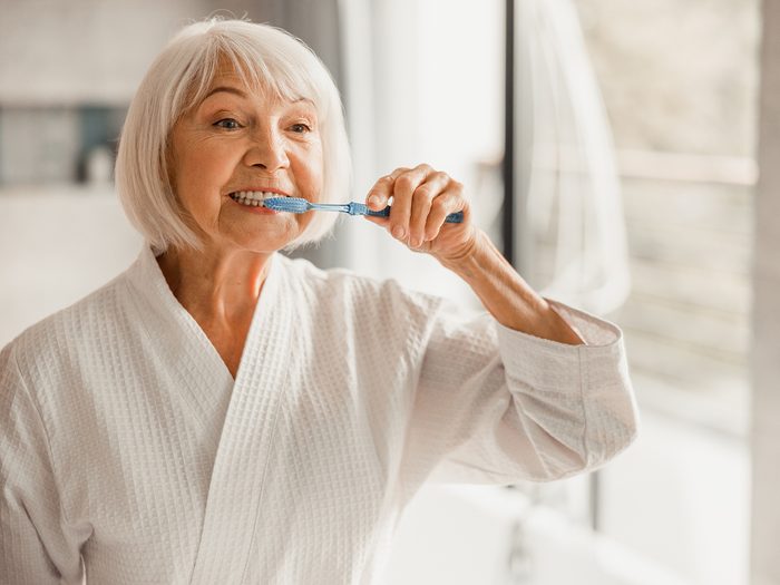 Signs of disease your teeth can reveal - mature woman brushing teeth