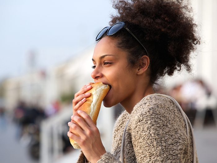 Reasons you're dehydrated - young woman eating sandwich