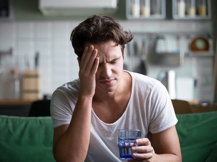 Sneaky reasons you're dehydrated - man with headache holding glass of water