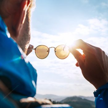 Backpacker man looking at bright sun through polarized sunglasses enjoying mountain landscape. Eye & Vision Care human health concept image.
