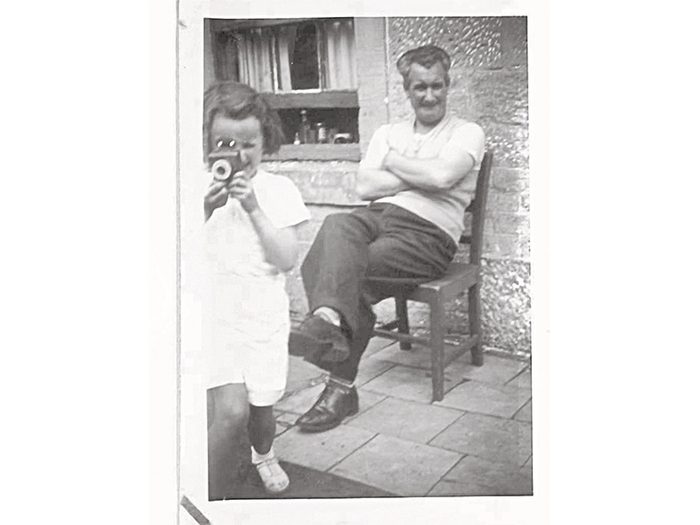 Ann as a child, camera in hand, with a smiling Papa seated behind her