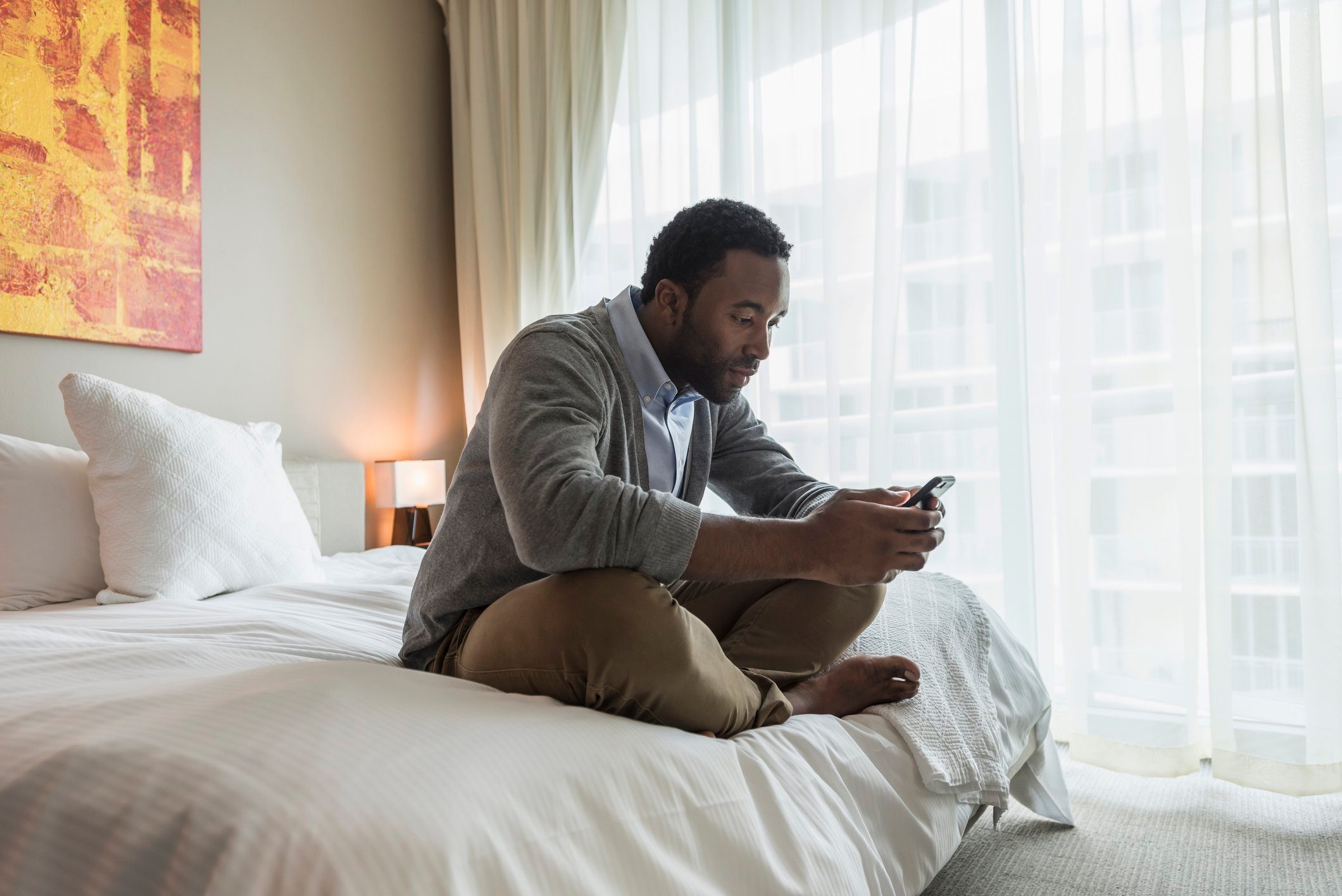 Black man using cell phone on bed