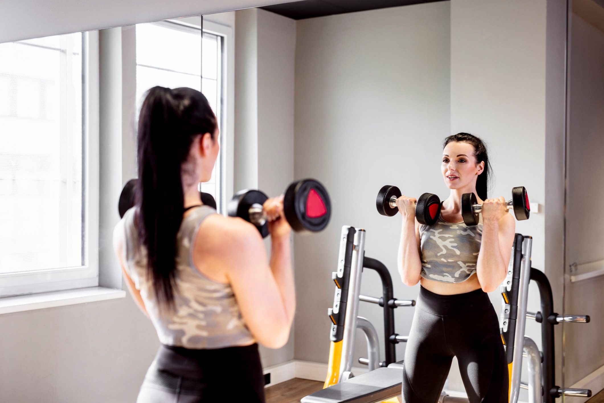 woman looking in mirror at gym while strength training