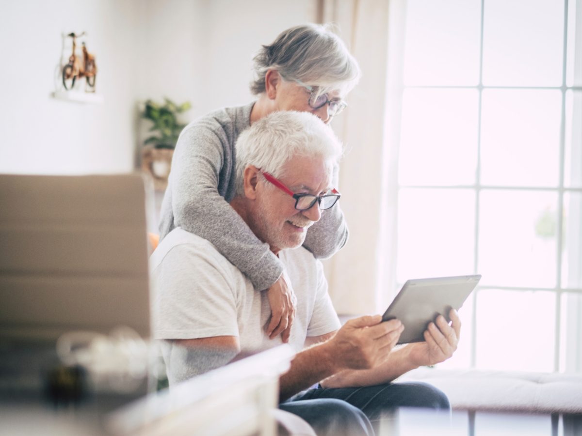 Senior couple using the laptop together at home in the kitchen - Covid