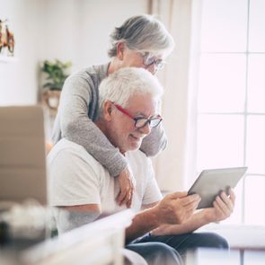 Senior couple using the laptop together at home in the kitchen - Covid