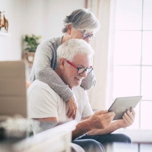Senior couple using the laptop together at home in the kitchen - Covid