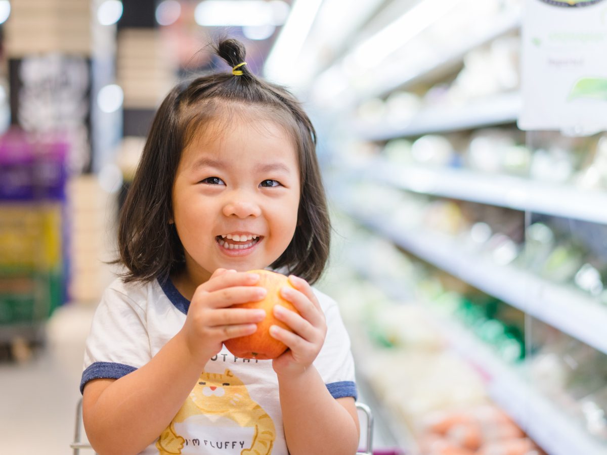 Cute little girl holding an apple in a supermarket