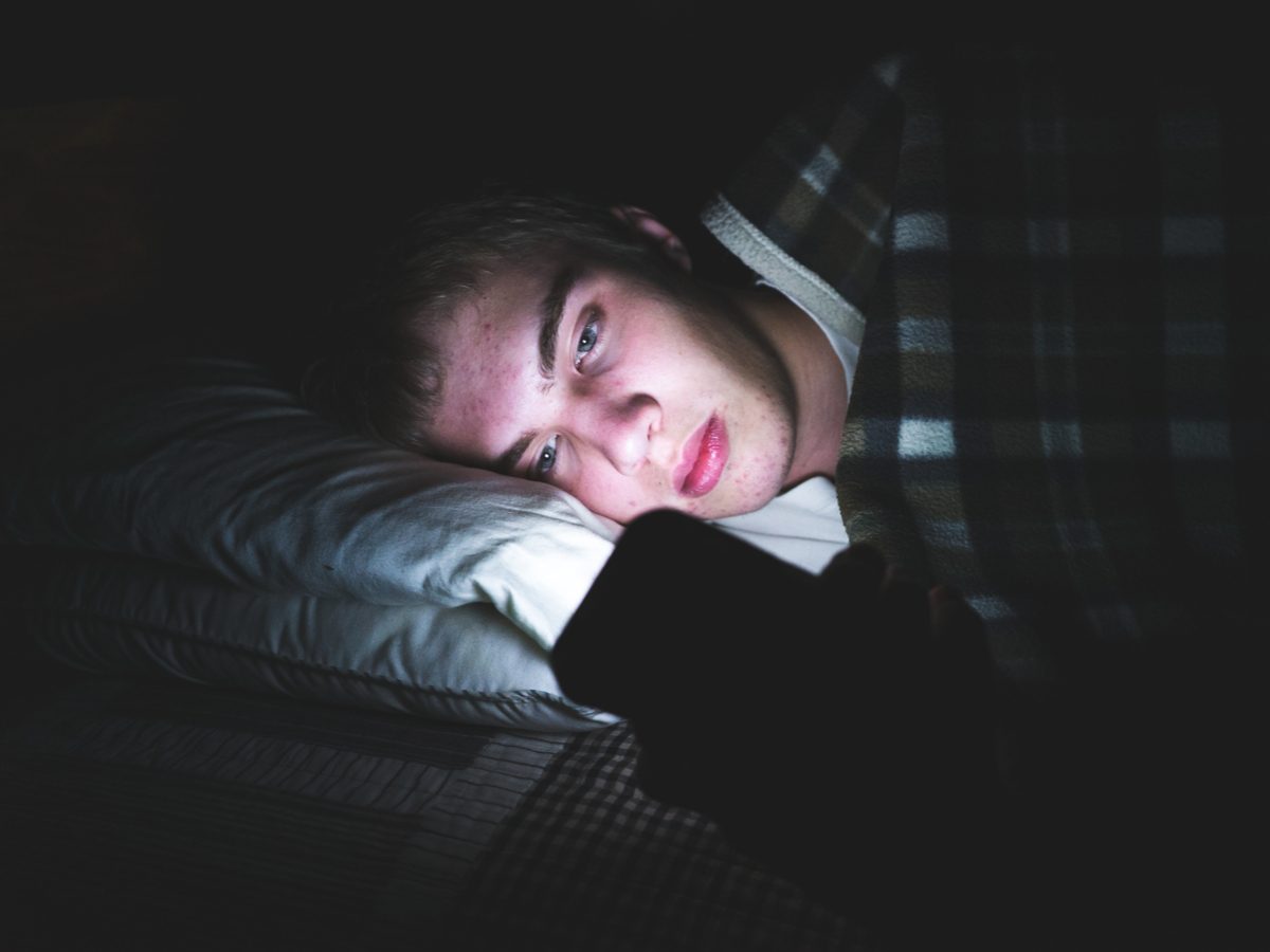 Teenage boy using his smartphone while in bed at night