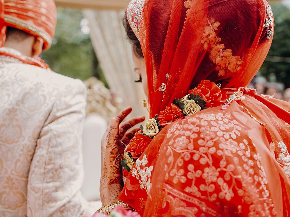 Look from behind at stunning Indian bride dressed in red lehenga and veil