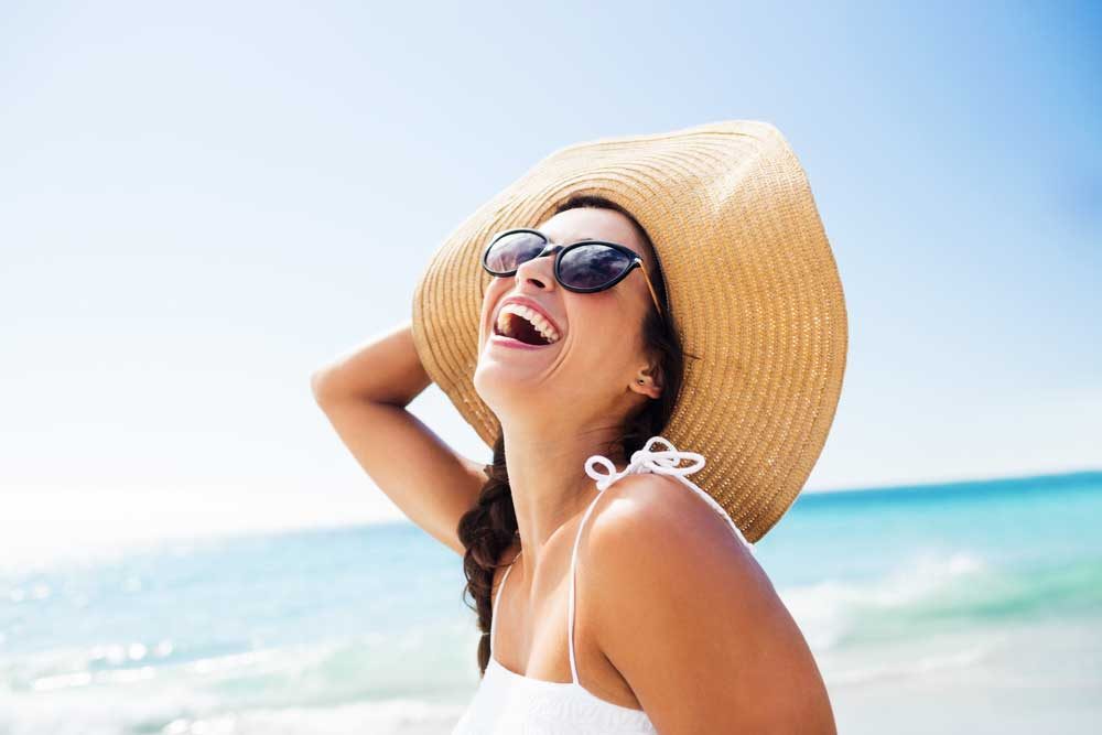 woman in sun hat, laughing at beach