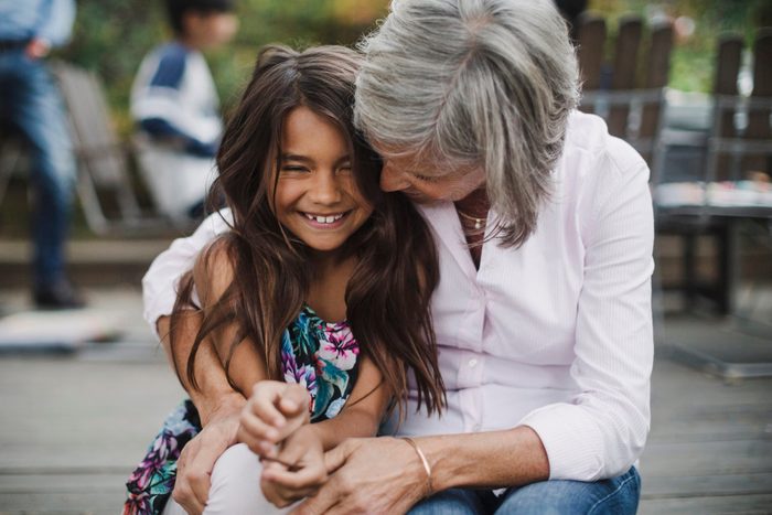 Senior woman embracing granddaughter while sitting at yard