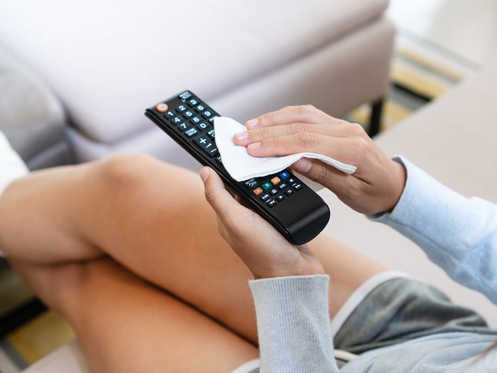 Tips from professional cleaners - woman hands cleaning the tv remote control with disinfectant wet wipes. Prevention of bacteria and covid-19 virus spreading concept.