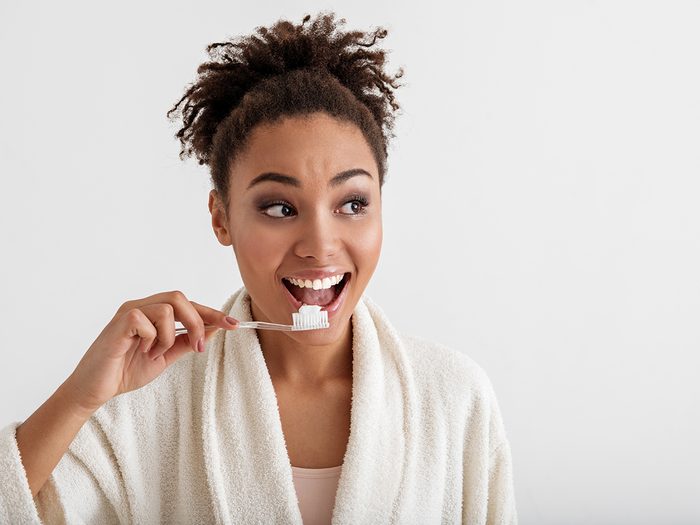 Brain exercises - Portrait of smiling girl brushing teeth. She is wearing housecoat and looking aside with happiness. Copy space in right side. Isolated on background