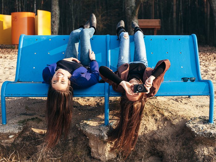 Brain exercises - Two funky friends making pictures lying upside down on a bench on the beach. Outdoor lifestyle portrait