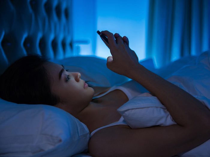 Secrets to a good night's sleep - woman using phone in bed