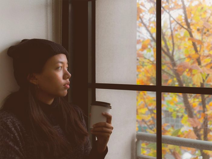 What is autumn anxiety? Young woman staring out of window in autumn