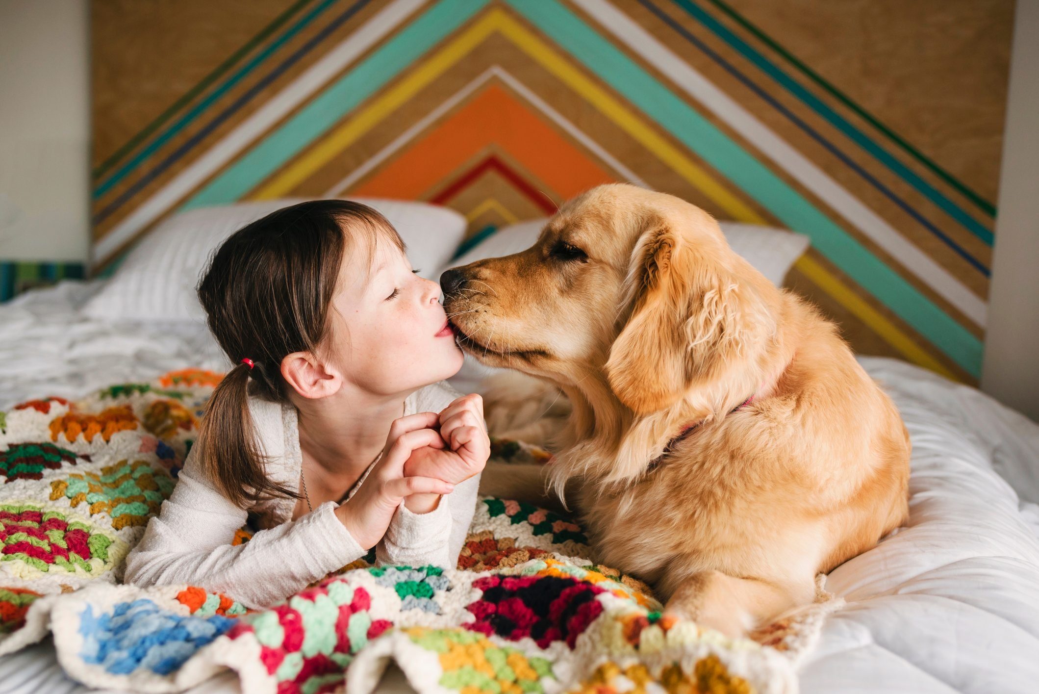 Most affectionate dog breeds - Girl lying on a bed kissing her golden retriever dog