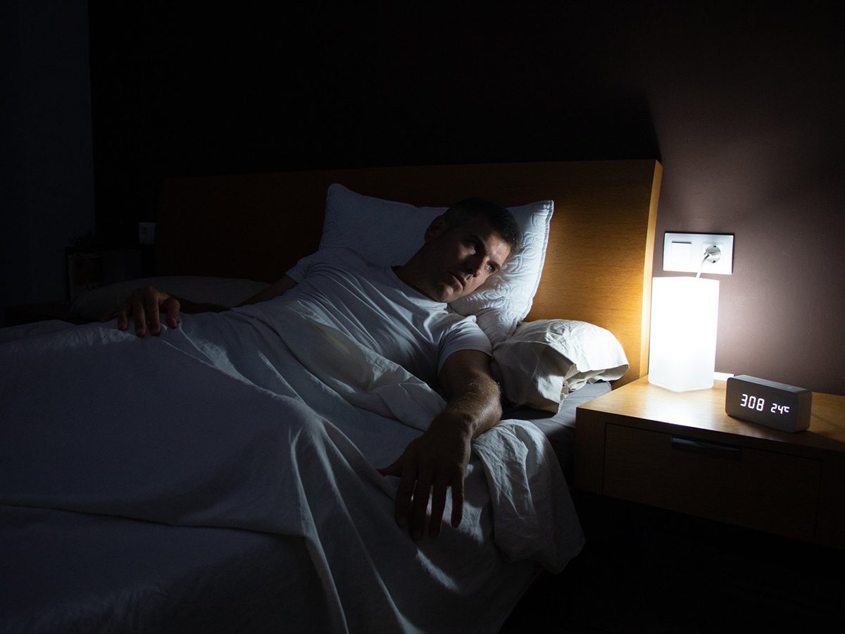 Anxiety at night - A man with insomnia looks at the clock at dawn from the bed with concern