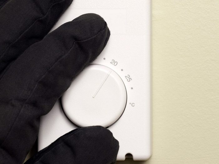 Best temperature for a house in winter - hand with glove changing thermostat