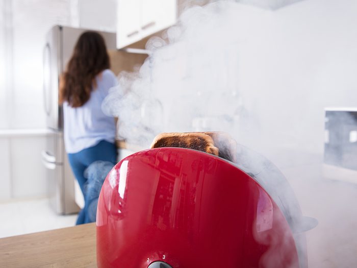 Close-up Of A Smoke Emitting Through Burnt Toast Coming Out From Red Toaster In Kitchen