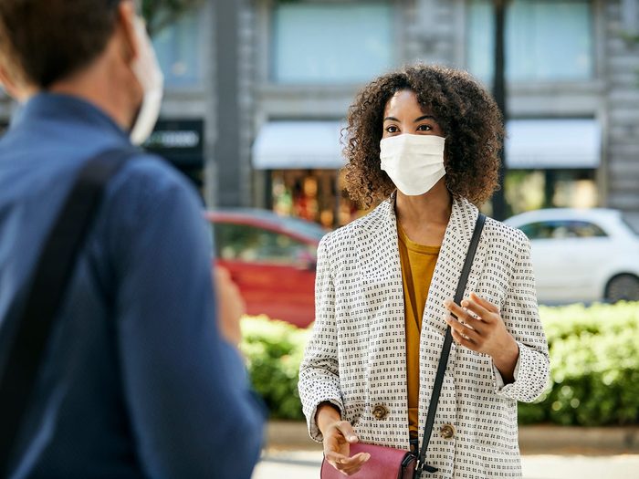 How to read people's face when they're wearing a mask - Businesswoman discussing with coworker in city. Female entrepreneur talking to male colleague during pandemic. They are maintaining social distance