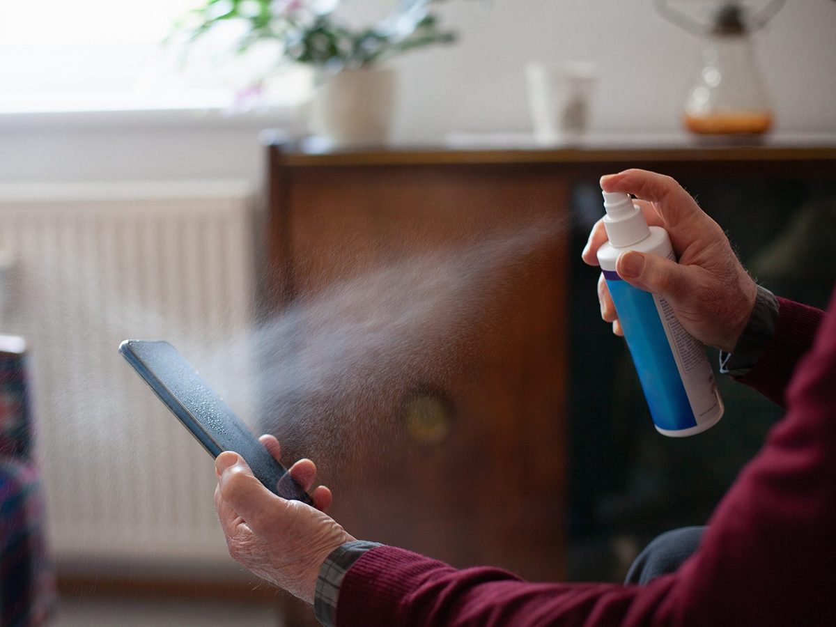 Mistakes you're making with disinfectant - Senior man obsessively cleaning his mobile phone with disinfectant spray, close-up of hands