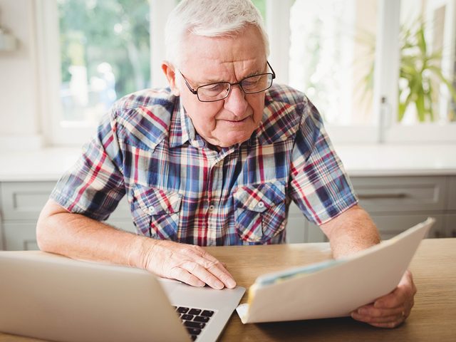 red flags someone is stealing your Wi-Fi - Worried senior man looking at a document while using laptop