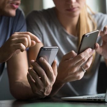 Close up view of man and woman using smartphones discussing mobile apps concept, couple talking holding cellphones synchronizing information online with laptop, checking news or texting messages