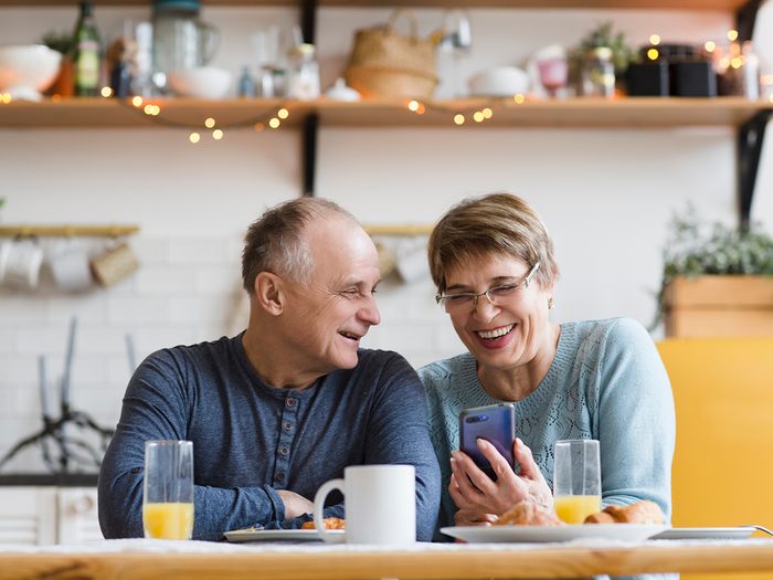 Senior couple eating breakfast and using smartphone at home