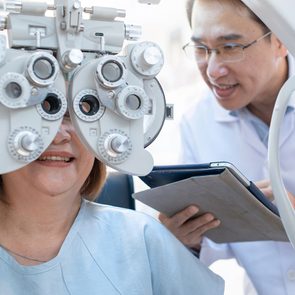 Eye doctor - Senior Asian woman looking through optical phoropter during eye exam,with an optometrist nearby
