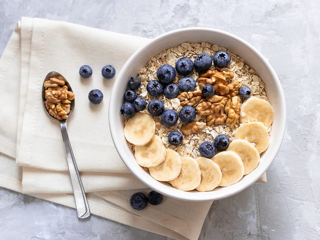 Oatmeal. Porridge with bananas, blueberries and walnut for healthy breakfast or lunch. Natural ingredients. Flat lay design on linen napkin and cement background