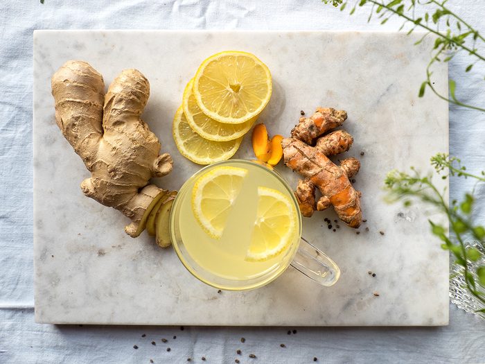 foods that prevent cancer - Marble board with immune system boosting ginger, lemon and turmeric hot tea on a set table.