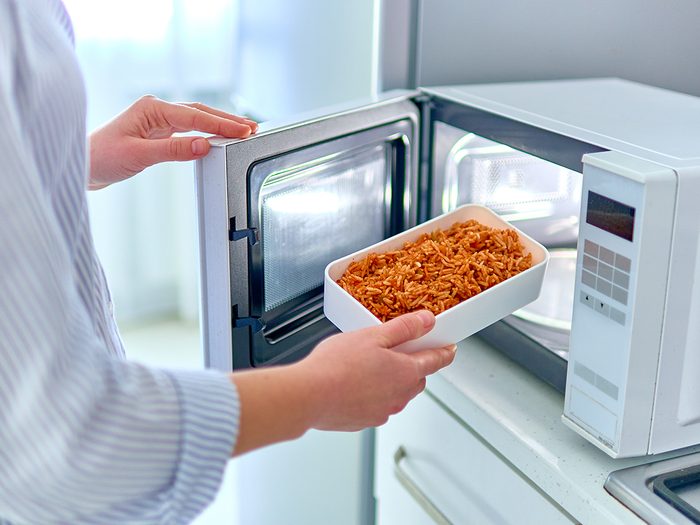 Woman warming up a container of food in the modern microwave oven for snack lunch at home