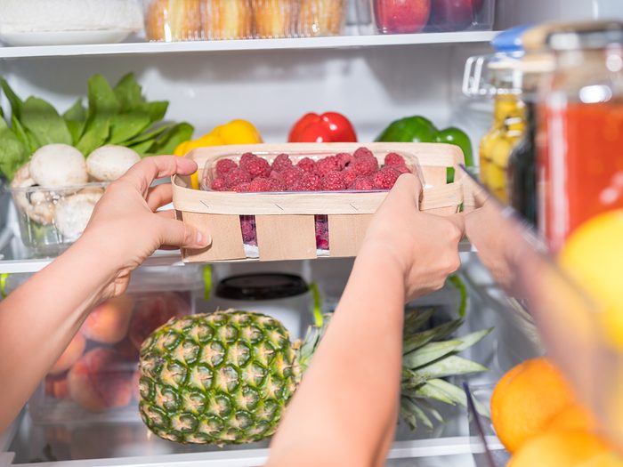 Person taking basket with fresh raspberries from open fridge
