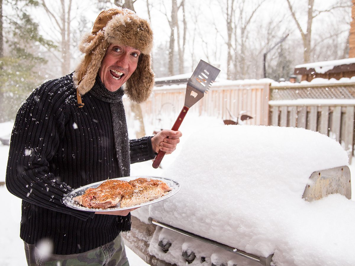 Winter grilling - man wearing winter hat with bbq in snow