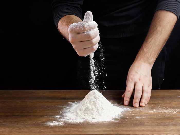 Cook sifting flour on countertop